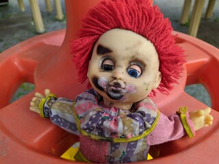 scary toy clown with red hair and half open blue eyes and outstretched hands in a plastic wheel
