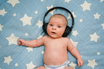 Bebe escuchando musica con cascos inalambricos sobre la cama con estrellas