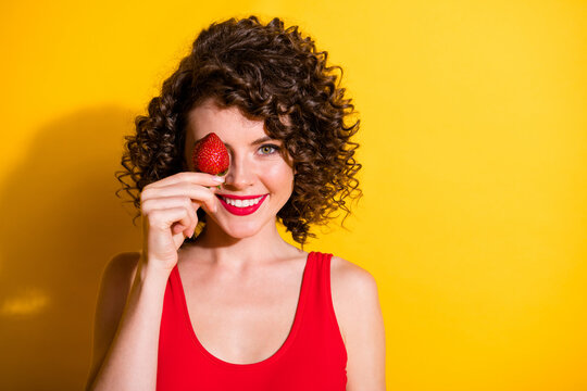 Photo of charming beaming lovely pretty childish wavy hairdo student lady healthy fruit diet empty space pretend strawberry eye wear bright red singlet isolated shine yellow color background - Powered by Adobe