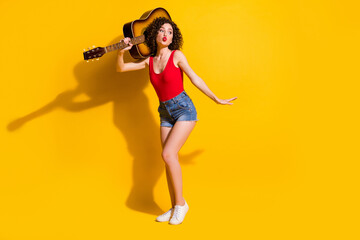 Fototapeta na wymiar Full length body size photo of pretty girl with curly hair holding keeping acoustic guitar bass sending air kiss with plump pouted lips isolated on vivid yellow color background