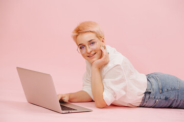 Happy woman with short hair lying on her stomach on the floor, working on laptop