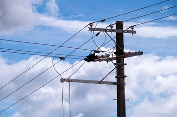 Electric wires and pole with white clouds and blue sky background.
