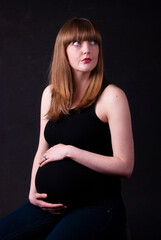 Portrait of a thoughtful pregnant woman with a black background, looking away from camera.