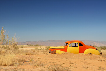 Rusty orange and yellow car wreck abandoned in the African desert. Landscape format.