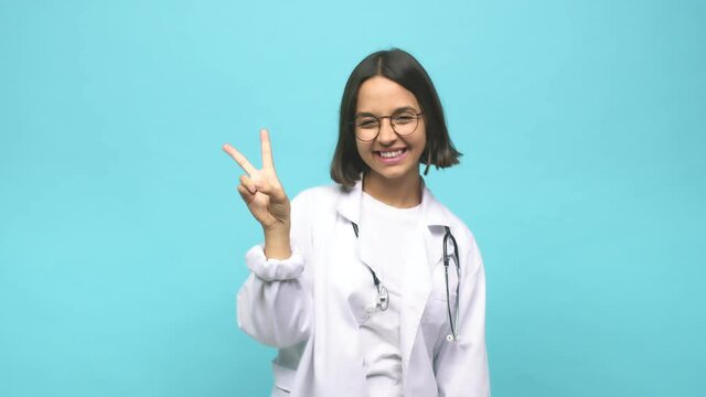 Young doctor indian woman joyful and carefree showing a peace symbol with fingers