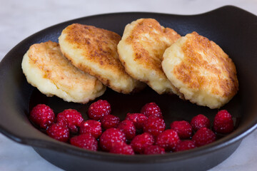 Close up fried homemade syrniki with fresh raspberry on black plate on white background