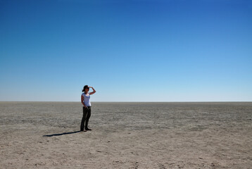 Woman looking out into the distance of the wide open space at the endorheic salt pan, Etosha pan, Namibia, Africa. 