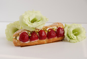 French pastry eclair with flowers, strawberry cake with cream and summer flowers on a white table,...