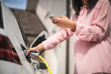 Woman charging electric car and making time adjustment on a smartphone