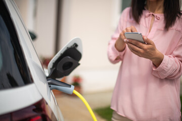 Woman charging electric car and making time adjustment on a smartphone