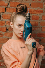 Girl with a drill stands against a background of a brick wall