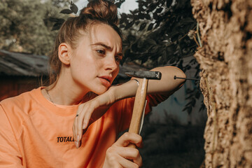 Tired girl hammering a nail into a tree