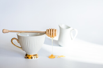 White cup with stick for honey Fresh honey flowing on table with wooden honeysbast.