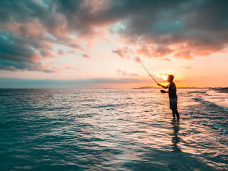 Fototapeta premium Silhouette of fishing off a beach at sunset