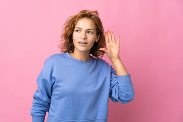 Fototapeta premium Young Georgian woman isolated on pink background listening to something by putting hand on the ear