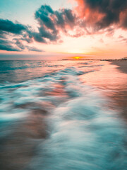Oceaanzonsondergang, langzame sluitertijd, golven die over het zand aanspoelen. Sterke zonsondergangkleuren en wolken boven de horizon