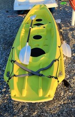 yellow kayak moored on the stony coast - afternoon shadows generated by sunlight - oars lying on the kayak - adventure sports to explore the waters - summer
