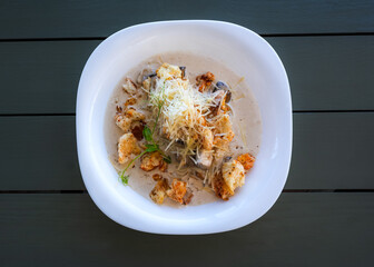 Puree soup with cheese and mushrooms. Hot soup with croutons and grated cheese on a white plate top view. Ready meal in a restaurant. Light lunch. Italian soup. Dark grey wooden background.