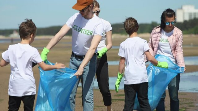 children help people volunteers to pick plastic rubbish and put in bag Spbi. kids collect bottles and rubbish on coast. teamwork of activists in t-shirt. ecology responsible people cleanup in gloves