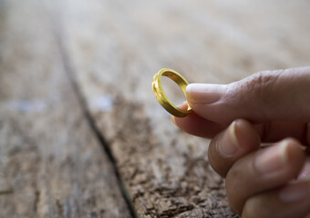 Broken heart concept. Close up hand holding gold ring, engagement ring on wood background.