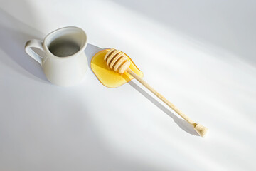 wooden stick for honey in puddle of yellow liquid spring honey. honeys remove on white background with spot of light.