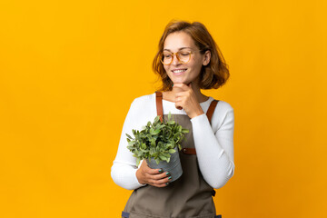 Young Georgian woman holding a plant isolated on yellow background looking to the side and smiling