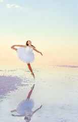 Fototapeta na wymiar Young girl ballerina makes jumps in the water of a salt lake. Reflection of a ballerina in the water. 