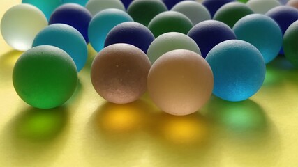 Blue and green glass frosted balls on a yellow surface. Partially defocused. Tactile play or...