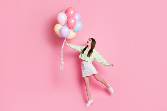 Full body photo of surprised shocked crazy cheerful girl hold many air balloons fly air impressed enjoy rejoice wear white sweater sneakers isolated pastel color background - Powered by Adobe