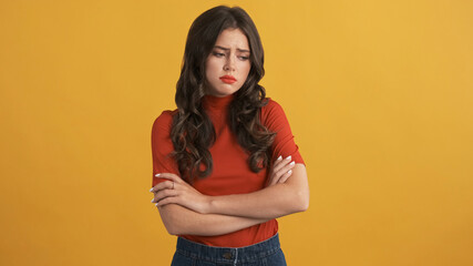 Offended girl in red top with hands crossed sadly posing on camera over colorful background