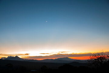 Sunrise in Guatemala, Moon high in the sky and volcanoes with mountains in silhouette.