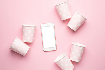 Mobile phone and polka dot disposable paper cups on pink background
