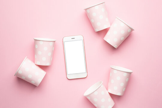 Mobile phone and polka dot disposable paper cups on pink background