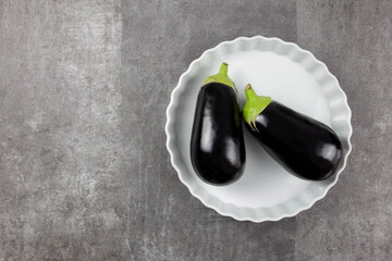 White ceramic baking dish on a dark background with eggplant, autumn vegetable.Food cooking background in an oven for your text. Top view. Copy space.