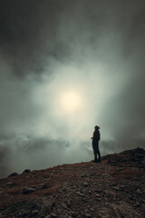 Man silhouette standing in front of sun and fog on the mountain