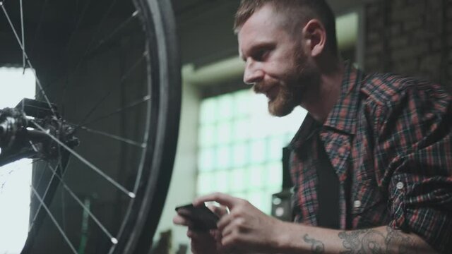Cyclist in a workshop, a garge takes a photo with a smartphone.