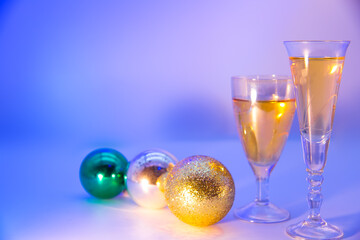Christmas background. Spruce green branches. New Year's toys hang on fir branches. Glasses with a drink. Beautiful colored lighting.