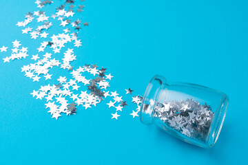 Glass jar with scattered confetti on blue background