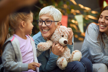 grandmother holding teddy bear, playing with her granddaughter