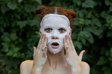 Beautiful woman anti-aging mask Surprised to touch your face with your hands bare shoulders bushes in the background