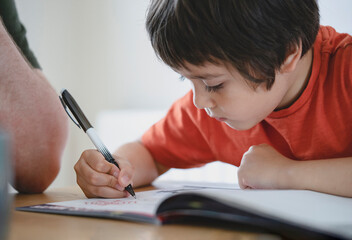Cropped shot father helping his boy with homework, Dad and Son doing homework together, Teacher teaching little boy how to write. Man hand holding pen, homeschooling concept