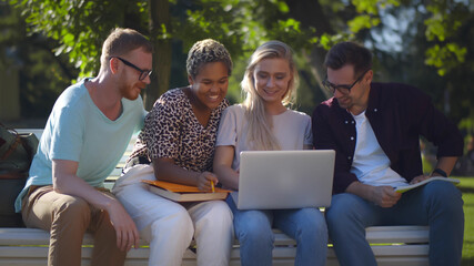 Multiethnic College Friends Relaxing After Classes Sitting Together On Bench Outdoors In Park