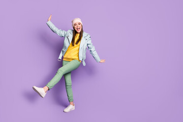 Full length photo of charming funky lady spring weather nice day street clothes good mood walk raise leg arms wear casual hat modern jacket pants shoes isolated purple color background