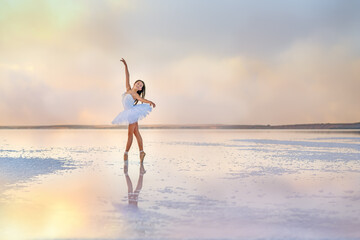 Fototapeta na wymiar A beautiful young ballerina dancing in the water of the lake with the reflection of clouds.