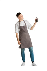 Shaker. Portrait of a young male caucasian barista or bartender in brown apron smiling. Studio white background, copyspace. Holding cocktails, inviting guests. Professional occupation, drink, service.