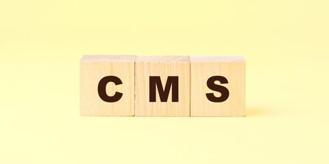 black letters cms written on wooden cubes against yellow