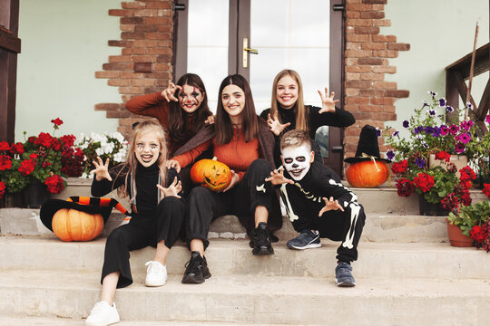 Happy kids celebrate halloween on the street near the house in costumes and make-up with pumpkin lantern jack, looking at the camera and having fun