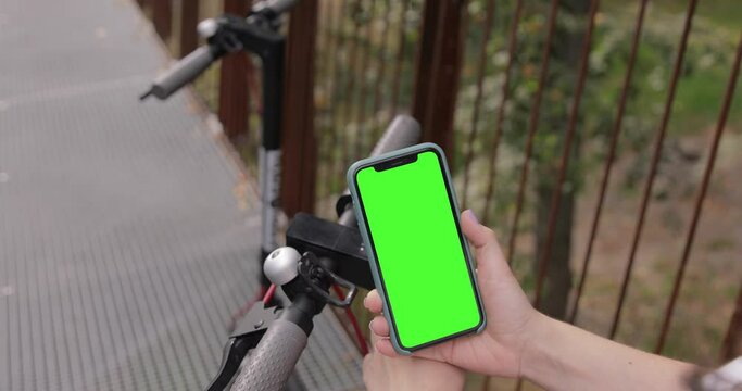Woman is unlocking rent bike using mobile phone iPhone 11 with pre keyed green screen. Electric scooter sharing business project