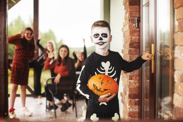 Boy and children in costumes and festive makeup with pumpkin lantern Jack knocking on the door for sweets at a halloween party on the street near the house