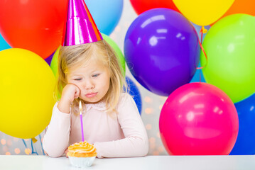 Sad little girl wearing  party's cap sits with birthday cupcake
